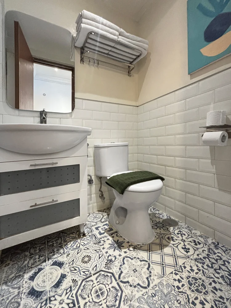 Santorini: Bathroom with basin, toilet and patterned floor tiles; the same soap and shampoo in every unit.
