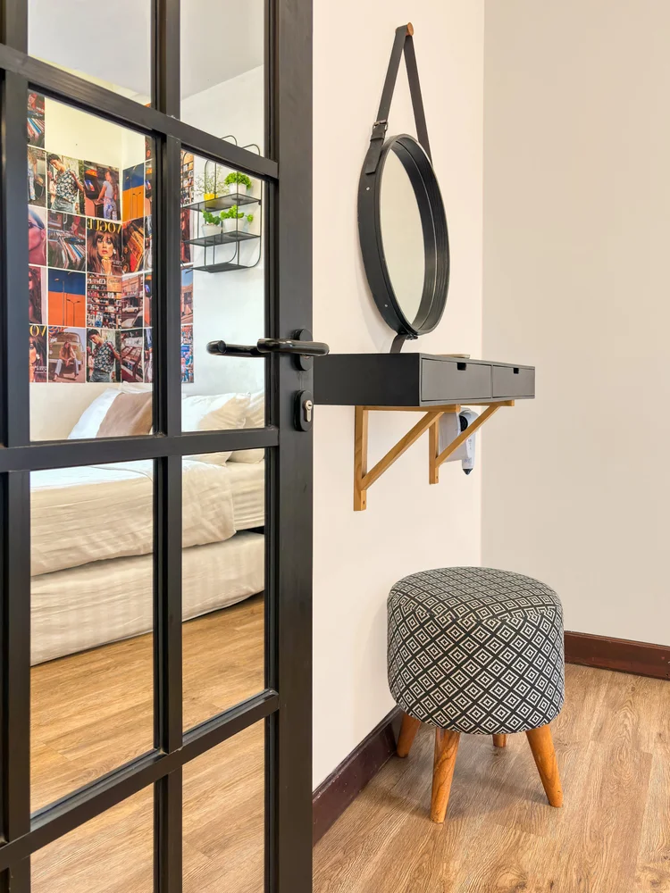 Brooklyn: A dressing shelf with round mirror and stool, behind the black-framed glass door.