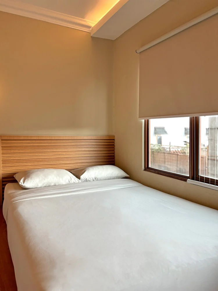 Nami: A bed by the window, with AC and roller blinds.