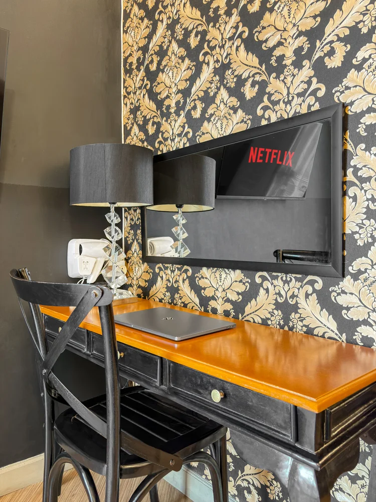 Vienna: Desk against black-and-gold damask wallpaper, a mirror TV with Netflix, and a hair dryer.