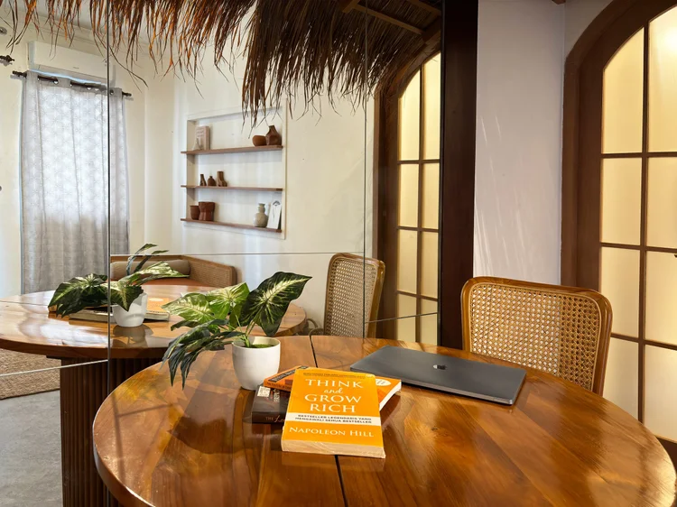 Ubud: A reading corner with a round wood table and rattan chairs, under the same thatched roof.