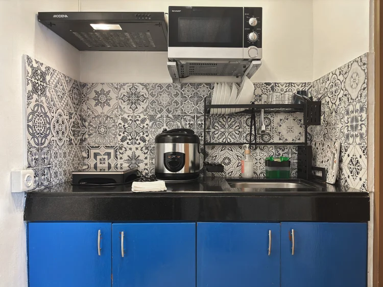 Santorini: Open kitchen with blue cabinets: induction stove, microwave, rice cooker and basic cooking tools.