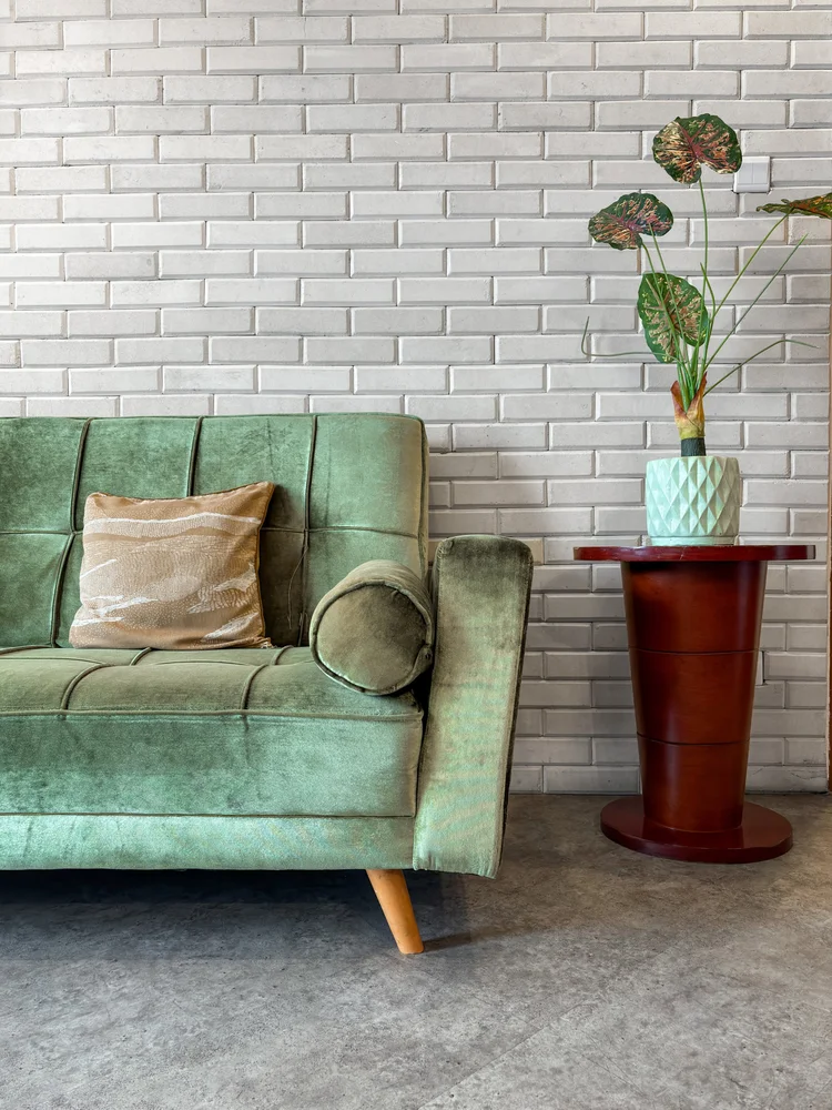 Chicago: The green sofa with cushions and a plant table, against the white brick wall.