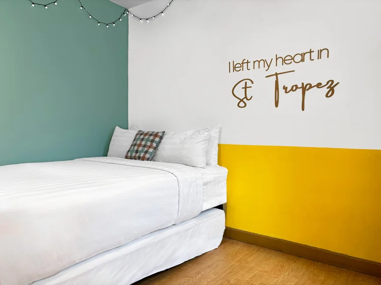 St. Tropez: The bed area with its wall lettering and string lights, white sheets as standard in all our units.