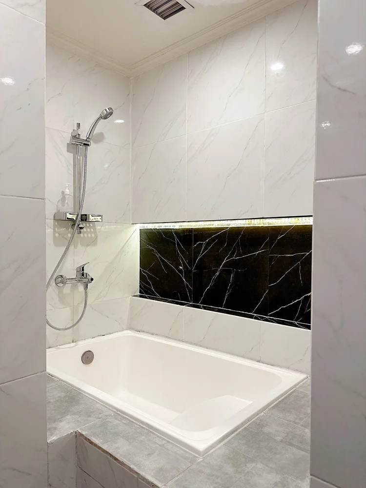 Boston: Bathtub with a hot-water shower, white marble look from floor to wall.