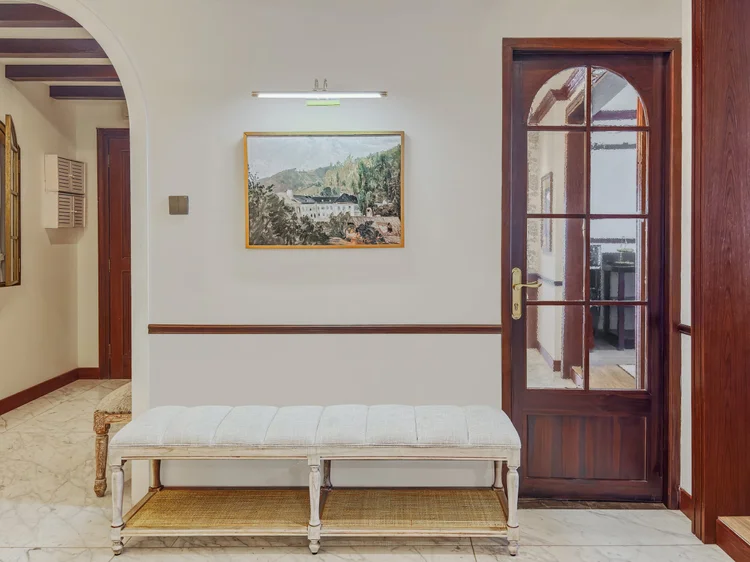 Kensington: A long hallway with a bench and a glass-paned door to a bedroom, classic style throughout.