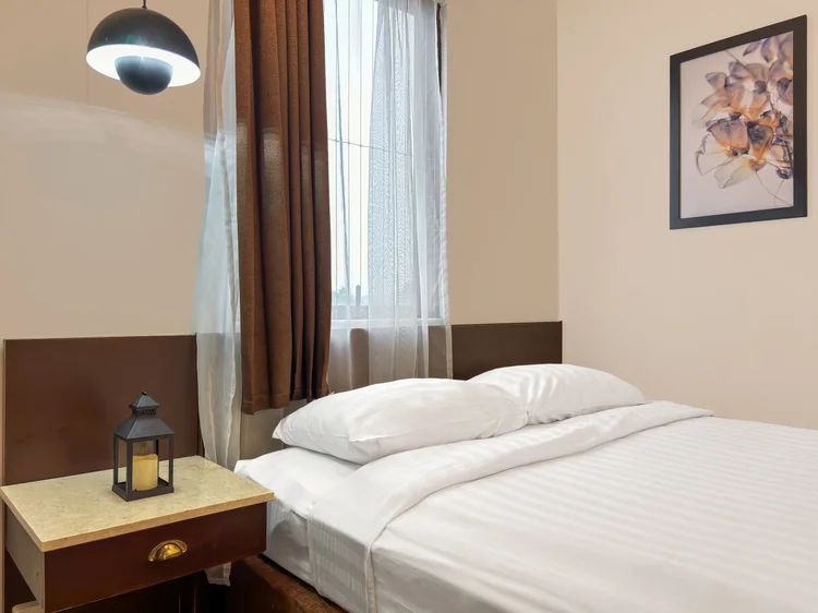 Norfolk: A bed with a small lantern lamp on the nightstand, thick curtains at the window.