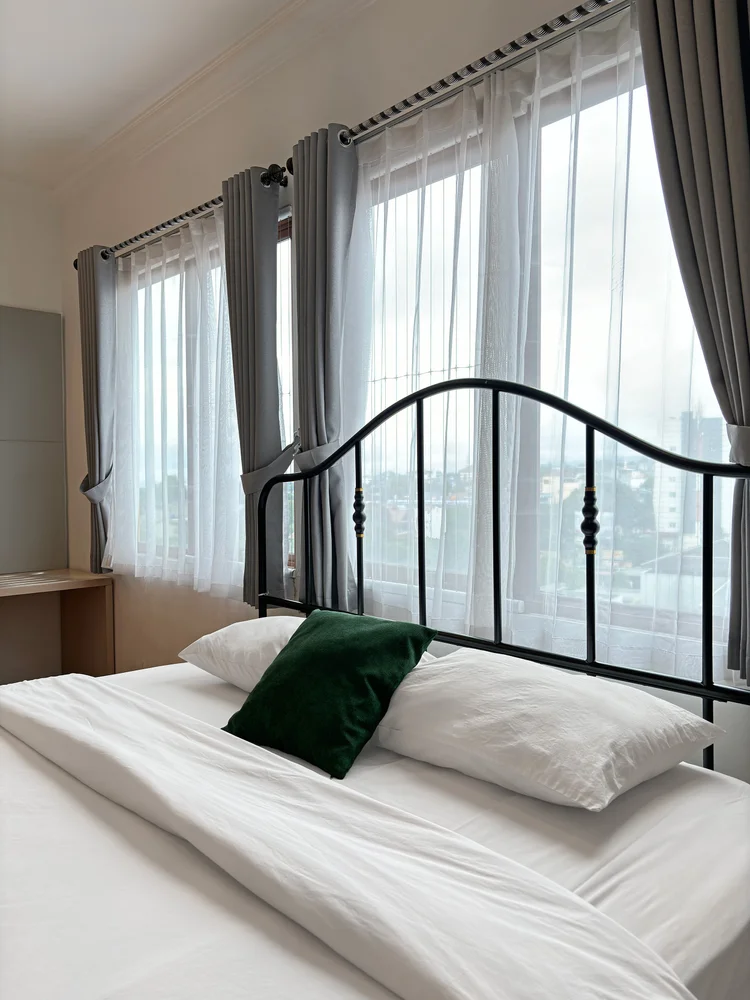 Paris: A Paris-style black iron bed, a curtained window at its head.